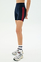 A person wears SPLITS59 Ella High Waist Airweight Short in Indigo/Pirate Red, paired with white socks and gray sneakers, standing against a plain white background.