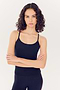 A young woman with curly hair wearing a SPLITS59 Airweight Tank in Indigo and leggings stands with her arms crossed, looking directly at the camera against a white background.
