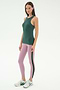 A woman stands against a plain background wearing the SPLITS59 Kiki Rib Tank Full Length in Military, light pink yoga leggings with a side stripe, and white athletic shoes—ideal for running or CrossFit workouts.