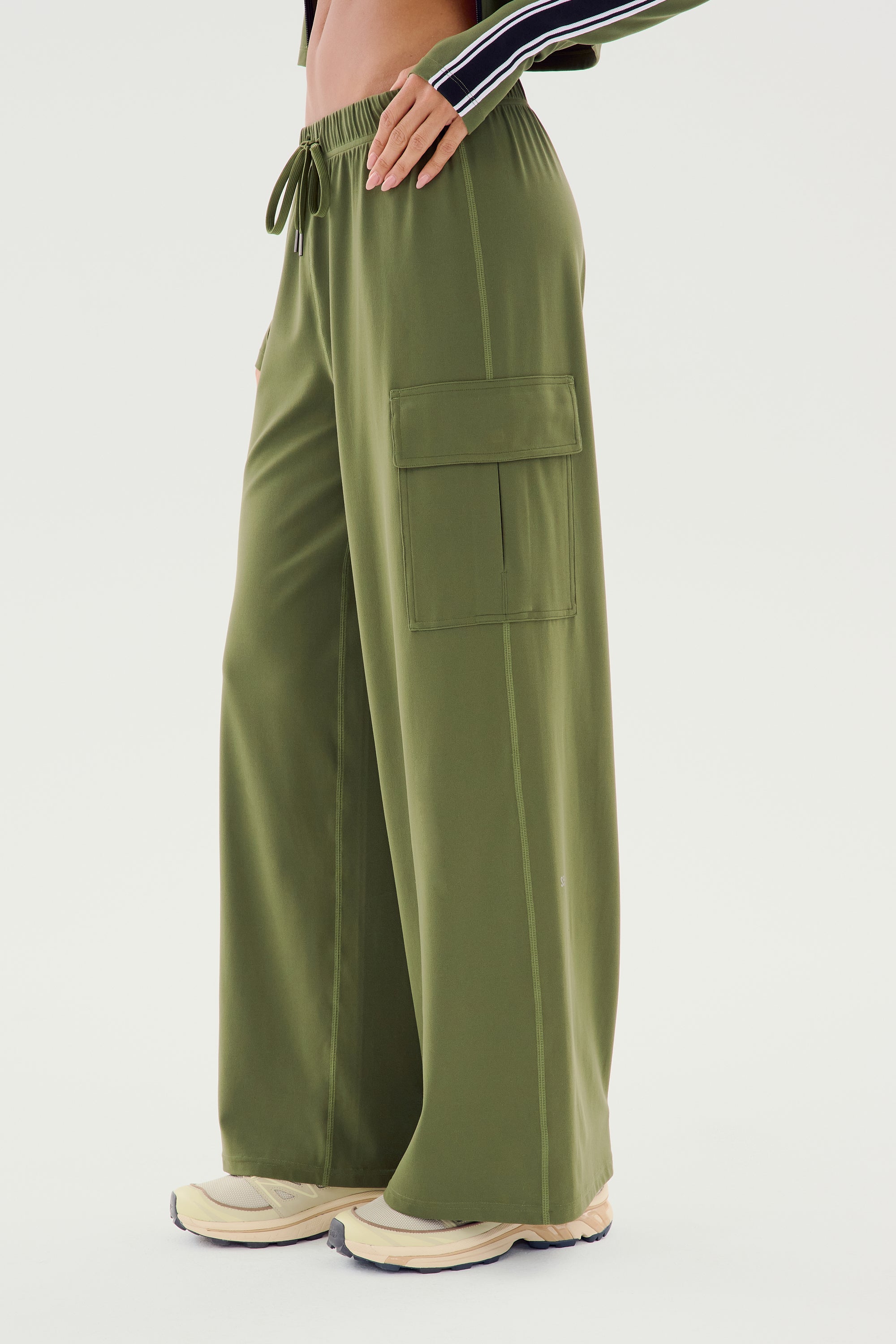 Person wearing the SPLITS59 Alex Airweight Cargo Pant in Olive, featuring a drawstring waist and side pockets made of durable nylon, paired with light-colored sneakers.