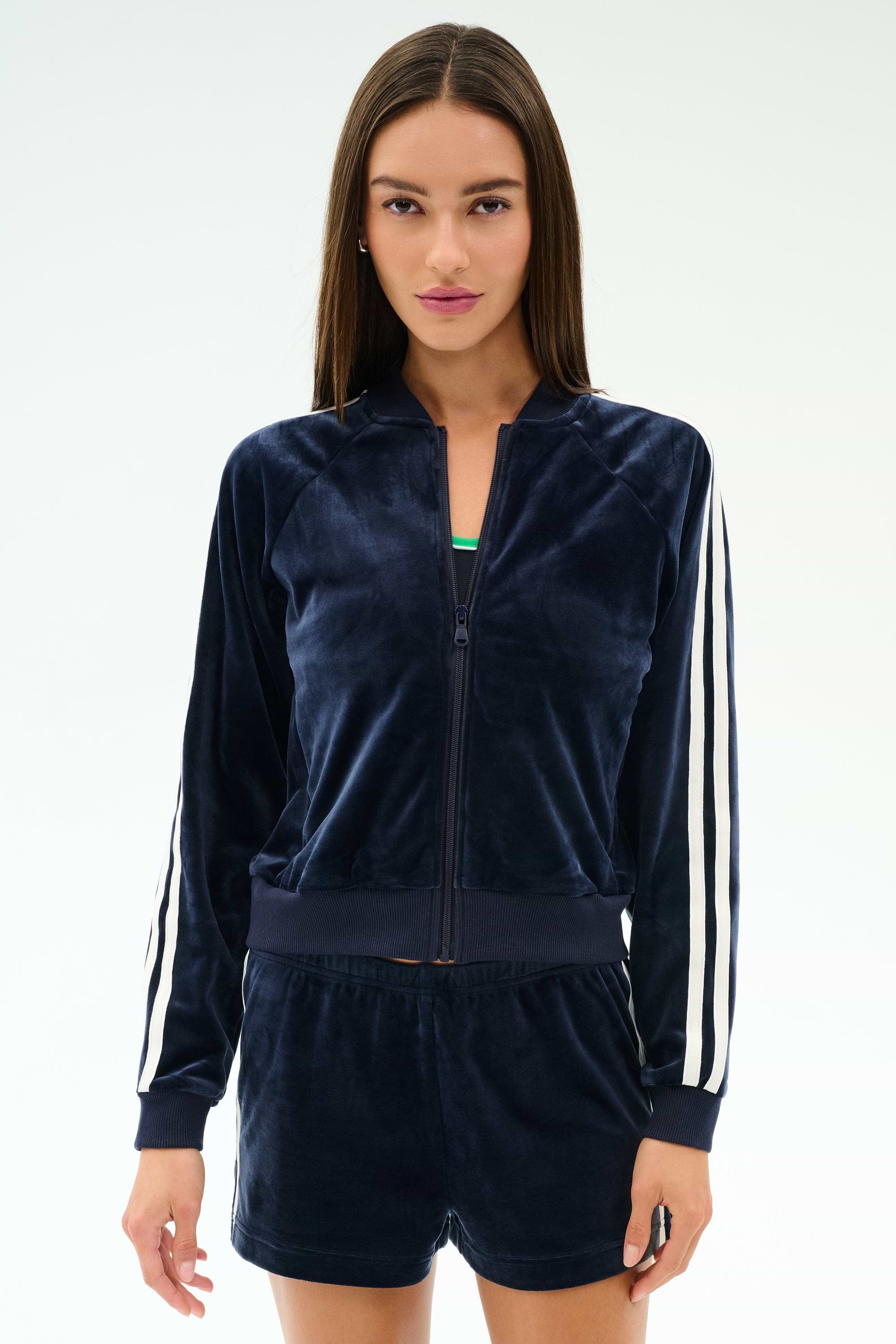 A woman faces forward wearing the SPLITS59 Heritage Velour Bomber in indigo/white, featuring white sleeve stripes and matching shorts.