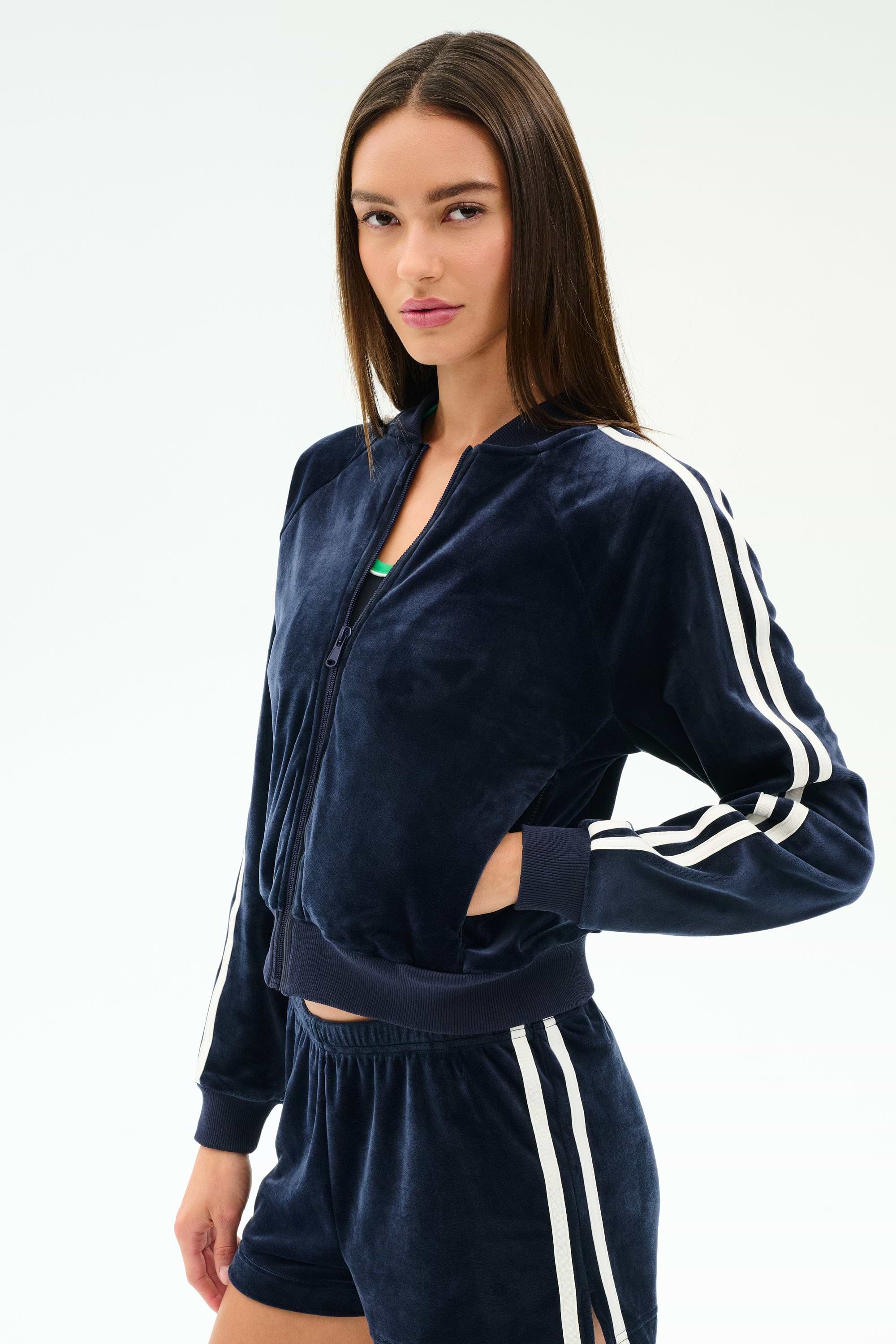A woman wears the SPLITS59 Heritage Velour Bomber in indigo/white, featuring white sleeve stripes, with matching shorts, standing against a plain white background.