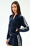 A woman wears the SPLITS59 Heritage Velour Bomber in indigo/white, featuring white sleeve stripes, with matching shorts, standing against a plain white background.