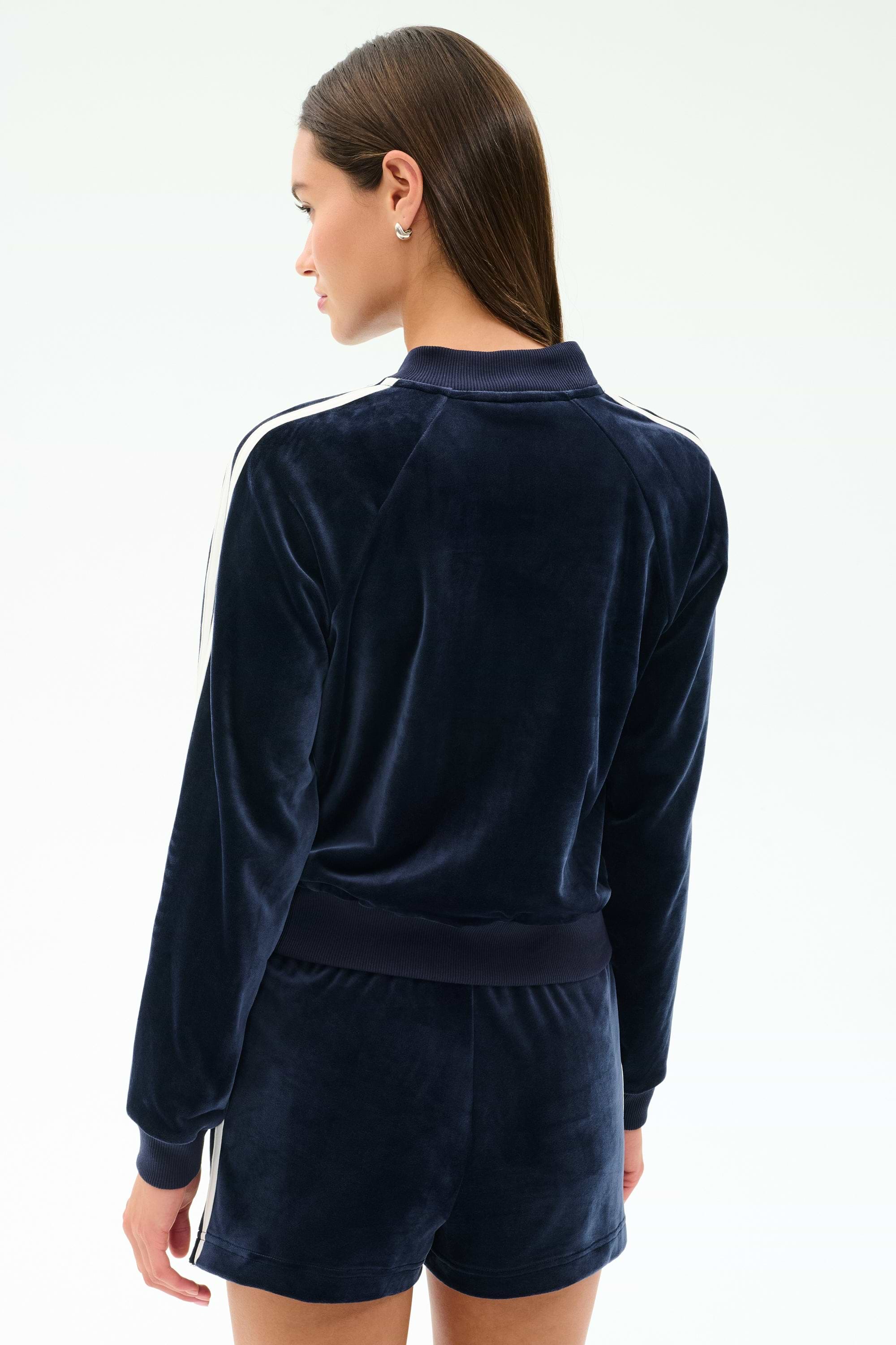 A woman is shown from the back wearing the SPLITS59 Heritage Velour Bomber in Indigo/White with matching shorts, featuring white stripes, against a plain background.