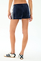 A person wearing SPLITS59 Heritage Velour Short in Indigo/White with white side stripes and white sneakers with navy accents, standing against a plain white background.