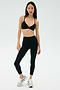 A woman wears the SPLITS59 Theo Rigor Bra - Black and high-waisted black leggings made from ultra-luxe Rigor fabric, paired with silver athletic shoes, standing against a plain light background.