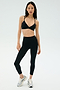 A woman wears the SPLITS59 Theo Rigor Bra - Black and high-waisted black leggings made from ultra-luxe Rigor fabric, paired with silver athletic shoes, standing against a plain light background.