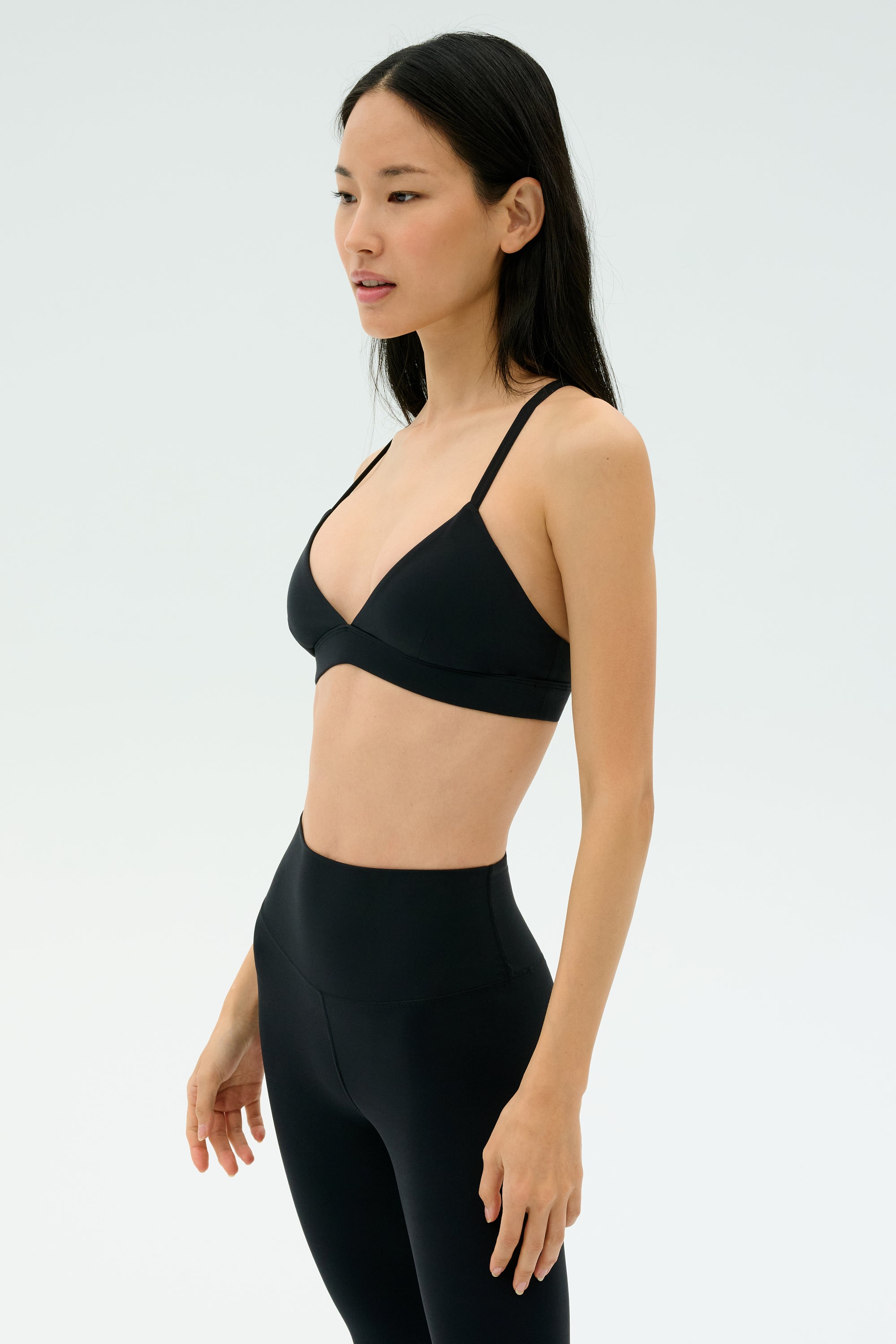 A woman in black SPLITS59 Theo Rigor Bra and high-waisted leggings, made from super soft Rigor fabric, stands against a plain light background.