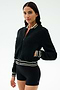 A woman stands against a plain background wearing the SPLITS59 Willa Sherpa Jacket in Black with striped cuffs and black fitted shorts—an ideal combo for winter workouts.