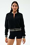 A woman wears the SPLITS59 Willa Sherpa Jacket in black, featuring a textured baseball style with striped trim, paired with black shorts, standing against a plain white background.