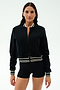 A woman wears the SPLITS59 Willa Sherpa Jacket in black, featuring a textured baseball style with striped trim, paired with black shorts, standing against a plain white background.
