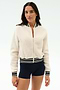 A woman wears the SPLITS59 Willa Sherpa Jacket in Creme with black and white striped trim and navy shorts, perfect for warming up before winter workouts, standing against a plain light background.