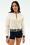 A woman wears the SPLITS59 Willa Sherpa Jacket in Creme with black and white striped trim and navy shorts, perfect for warming up before winter workouts, standing against a plain light background.