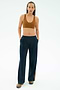 A person wears the SPLITS59 Airweight Scoop Back Bra in Honey, navy wide-leg pants with pockets, and brown sneakers against a plain light background.
