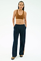 A person wears the SPLITS59 Airweight Scoop Back Bra in Honey, navy wide-leg pants with pockets, and brown sneakers against a plain light background.