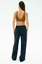 A person with braided hair stands facing away, wearing the SPLITS59 Airweight Scoop Back Bra in Honey and navy blue track pants with a stripe down the side.