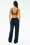 A person with braided hair stands facing away, wearing the SPLITS59 Airweight Scoop Back Bra in Honey and navy blue track pants with a stripe down the side.