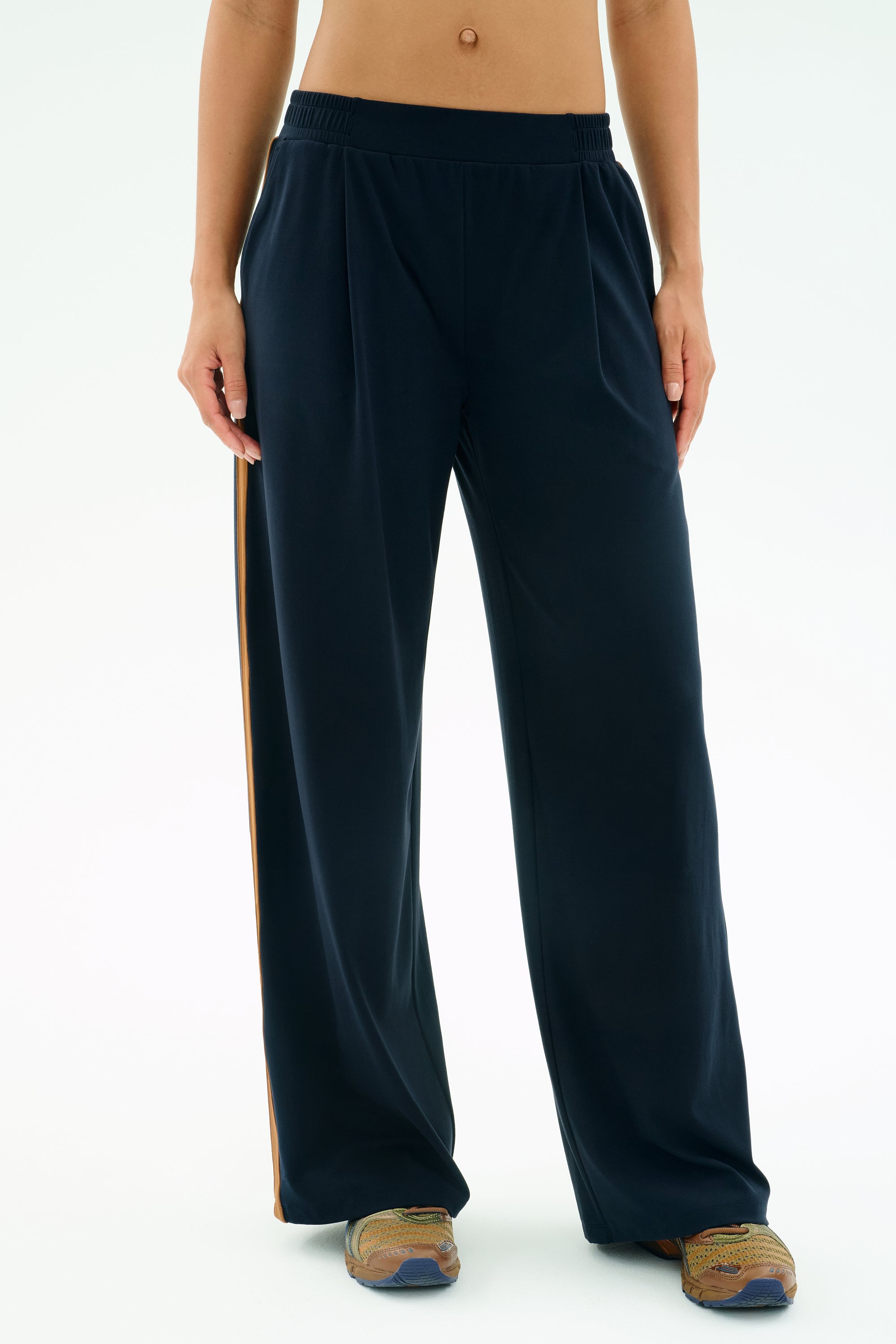 A person wearing SPLITS59's Luca Airweight Trouser with Stripe in Indigo/Honey and multicolored sneakers stands against a plain background.