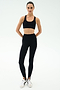 A person stands facing forward in a SPLITS59 Sara Airweight Bra - Black, black high-waisted leggings, and white sneakers—an ideal Pilates or hot yoga look—against a plain white background.