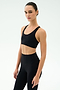 A woman in the SPLITS59 Sara Airweight Bra - Black and high-waisted leggings stands against a plain white backdrop, gazing at the camera—ideal activewear for Pilates or hot yoga.