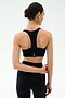 A woman with dark hair in a bun wears the SPLITS59 Sara Airweight Bra in black and matching leggings, standing with her back to the camera against a light background—ideal for Pilates or hot yoga.