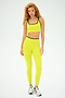A person with curly hair, wearing the SPLITS59 Easton Rigor High Waist 7/8 in Chartreuse/Black and silver sneakers, stands ready for gym workouts against a plain background.