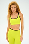 A person with curly hair wears the SPLITS59 Cait Rigor Bra in bright yellow, paired with leggings, against a plain background.