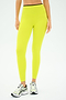 A person sports the SPLITS59 Easton Rigor High Waist 7/8 leggings in chartreuse/black, made from durable Rigor fabric, paired with sleek white sneakers against a plain backdrop.