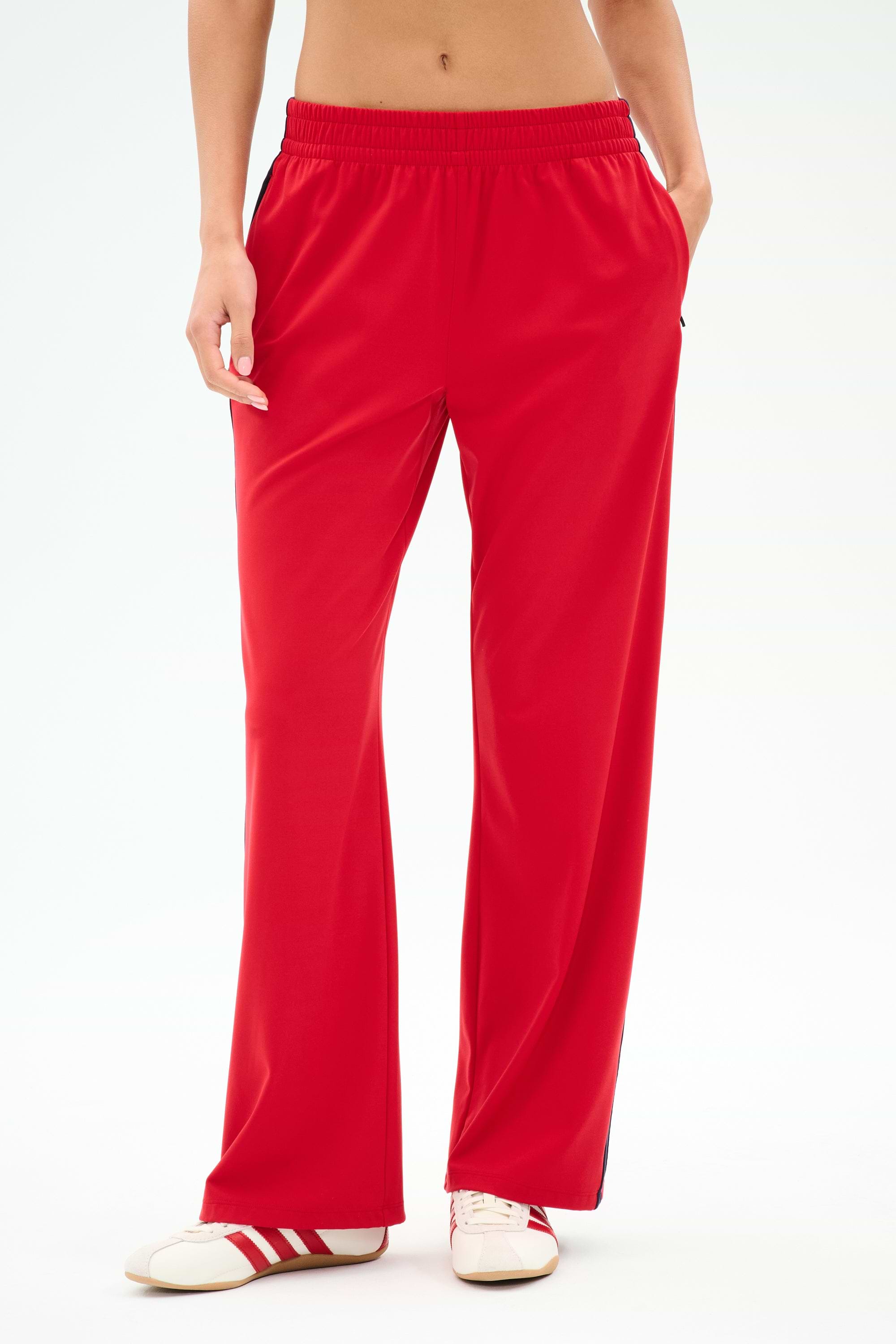 Model wears SPLITS59 Maxie Rigor Track Pant in Pirate Red/Indigo, wide leg style, paired with red-and-white sneakers, shown from waist to feet against a plain background.