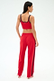 A woman faces away, wearing a red sports bra and SPLITS59 Maxie Rigor Track Pant in Pirate Red/Indigo—wide leg track pants with indigo trim—against a plain light background.