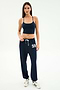 A woman stands against a plain background wearing the SPLITS59 Airweight Crop - Indigo with matching navy joggers featuring "59" on the thigh and white sneakers—a stylish look for hot yoga or casual outings.