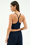 A woman stands with her back to the camera in the SPLITS59 Airweight Crop - Indigo, paired with matching pants against a plain light background—ideal attire for hot yoga sessions.