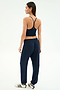 A woman faces away, wearing the SPLITS59 Airweight Crop in Indigo, matching indigo sweatpants, and white sneakers with indigo stripes against a plain white background.