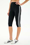 A person wears SPLITS59 Ella High Waist Airweight Capri in Black/White, featuring two white side stripes, paired with white sneakers with black accents, standing against a plain white background.