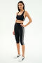 A woman stands in a studio wearing the SPLITS59 Ella High Waist Airweight Capri in Black/White, paired with a black sports bra and white athletic sneakers.