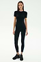 A woman faces forward against a white background wearing the SPLITS59 Louise Rib Short Sleeve in black, paired with black leggings featuring a blue side stripe and black sneakers.