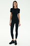 A woman faces forward against a white background wearing the SPLITS59 Louise Rib Short Sleeve in black, paired with black leggings featuring a blue side stripe and black sneakers.