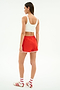 A woman faces away, wearing a white spandex sports bra and SPLITS59 Megan Woven Nylon Run Short in Lotus Red/Creme, paired with white socks with red stripes and white sneakers with red accents.