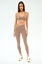 A woman faces the camera wearing the SPLITS59 Mia Rigor Bra in Latte, with matching high-waisted leggings and beige sneakers against a plain light background.