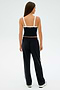 An individual is dressed in a black SPLITS59 sports top featuring white straps, paired with Maxie Rigor Track Pant - Black/White from SPLITS59, standing against a light background.