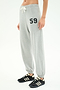 A person wearing SPLITS59 Andie Oversized Fleece Varsity 59 Sweatpant in Heather Grey/59, featuring "59" on the left thigh, white drawstring, and paired with black athletic shoes with white stripes.