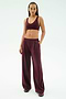 A woman stands against a white background wearing the SPLITS59 Airweight Scoop Back Bra in Dark Cherry, paired with wide-leg pants and sneakers, all made from soft nylon spandex for comfort and ease of movement.