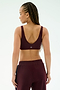 A person with braided hair is seen from the back wearing the SPLITS59 Airweight Scoop Back Bra in Dark Cherry, crafted from nylon spandex, against a light background.