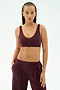 A woman wears the SPLITS59 Airweight Scoop Back Bra in Dark Cherry, made from soft nylon spandex, paired with matching pants and stands against a plain light background with one hand in her pocket.