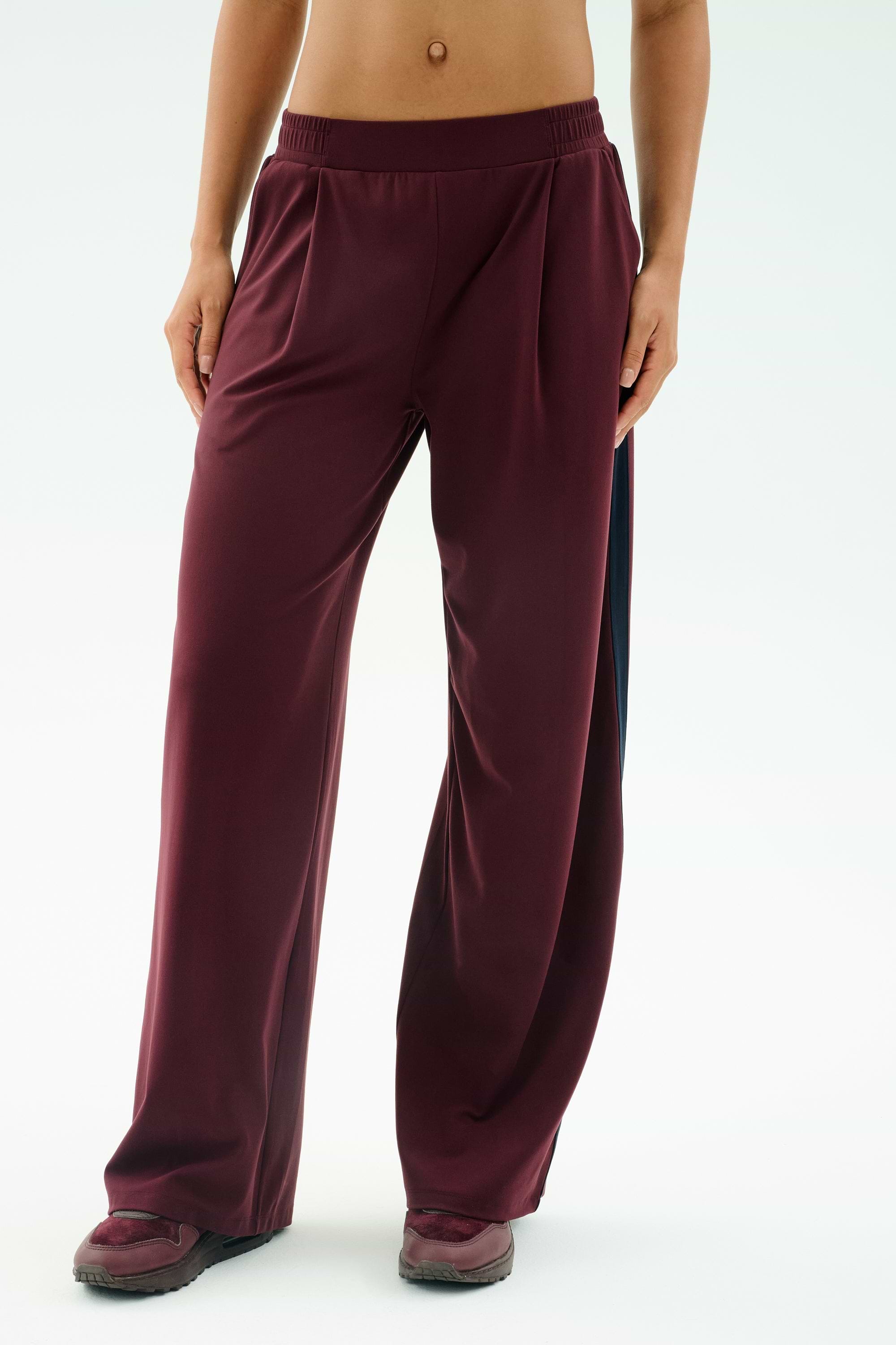 A person wearing SPLITS59's Luca Airweight Trouser with Stripe in Dark Cherry/Indigo, styled with matching maroon sneakers, shown from waist to feet against a plain background.