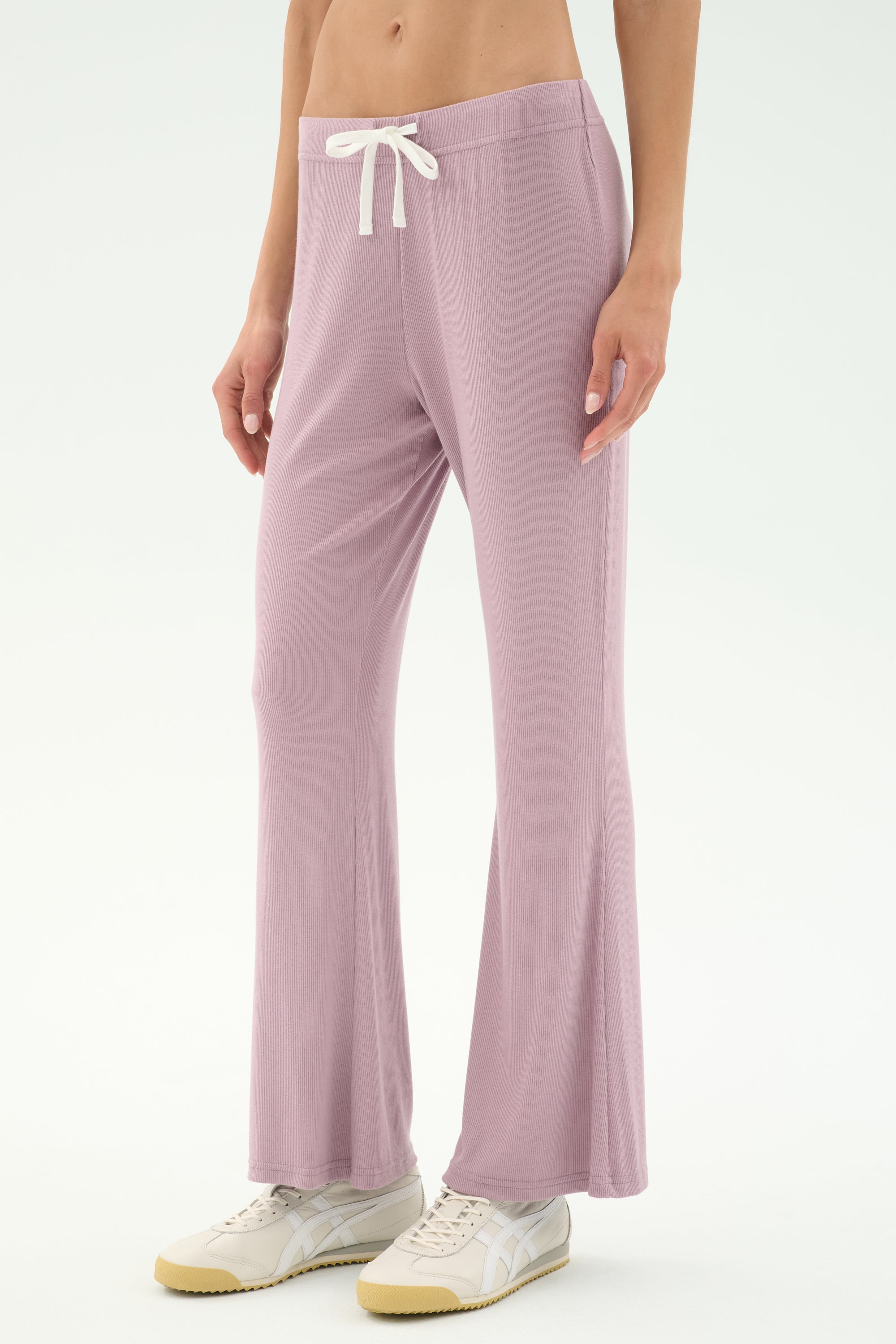 A person wears SPLITS59 Blaire Rib Pant in Blush, featuring soft modal fabric and a drawstring waist, paired with white sneakers against a plain light background.