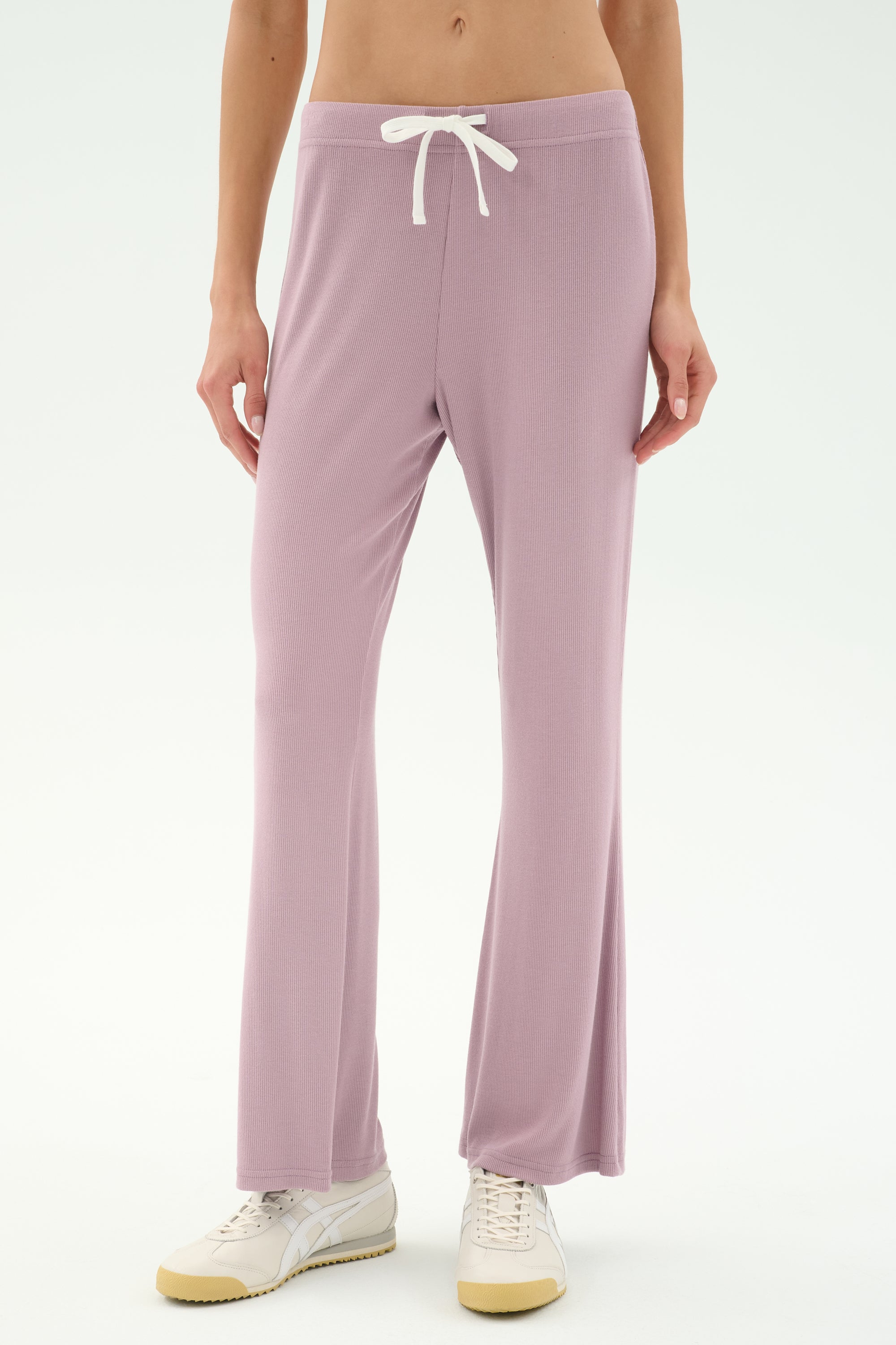 A person wears SPLITS59's Blaire Rib Pant in Blush, crafted from soft modal fabric, paired with white sneakers. Only the lower torso and legs are shown, standing against a plain light background.