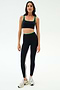A woman wears the SPLITS59 Cait Rigor Bra in Black/Grass—black with green trim—paired with matching high-waisted leggings in Rigor fabric, both featuring a white side stripe, standing against a white background.