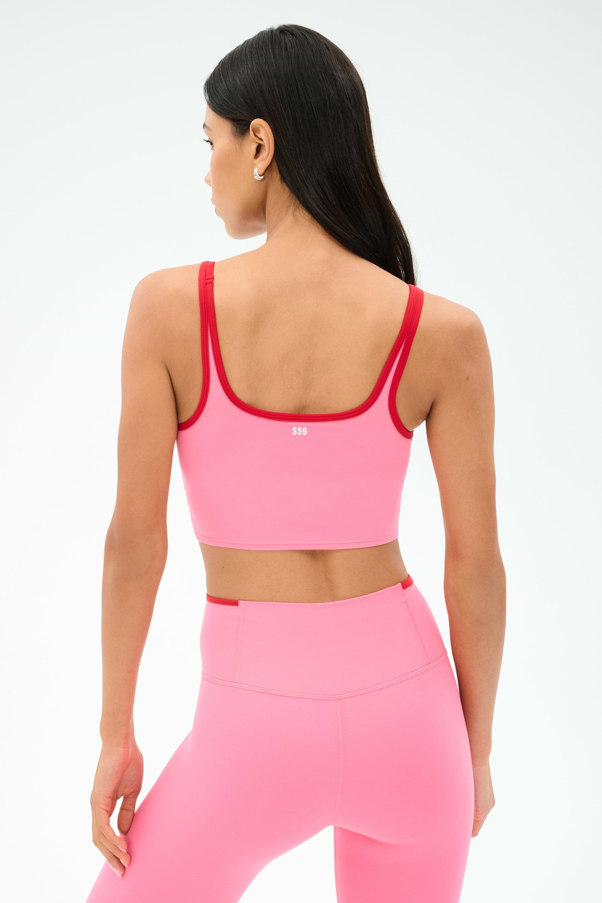 A woman with long dark hair is shown from the back against a plain light background wearing the SPLITS59 Cait Rigor Bralette in Strawberry/Pirate Red, paired with matching leggings, crafted from a soft nylon spandex blend.