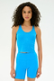 A woman with curly hair wears the SPLITS59 Ashby Rib Crop in blue and matching shorts, standing against a plain white background.